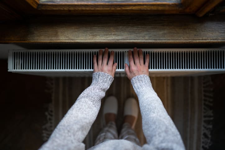 Woman in Sweater Next to Heater Vent